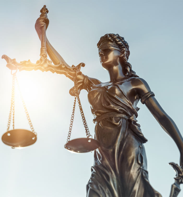 Bronzestatue der Justitia mit Waage vor hellem Himmel